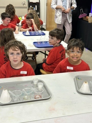 Picture of seven students sitting at tables wearing safety glasses with experiment trays in front of them.