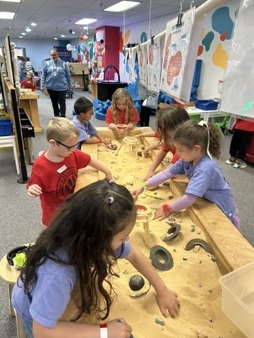 Picture of six students digging in a sand table .