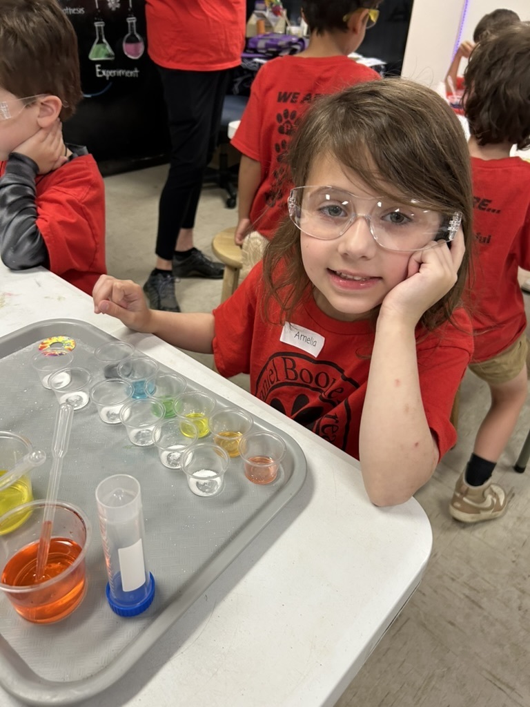 Picture of a student sitting in front of a tray with three plastic cups with droppers, a paper cone and smaller plastic 1 oz cups.