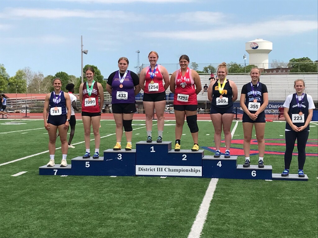 Eight students wearing number bibs and medals standing on a rising podium showing 1st - 8th place in the District III Championships