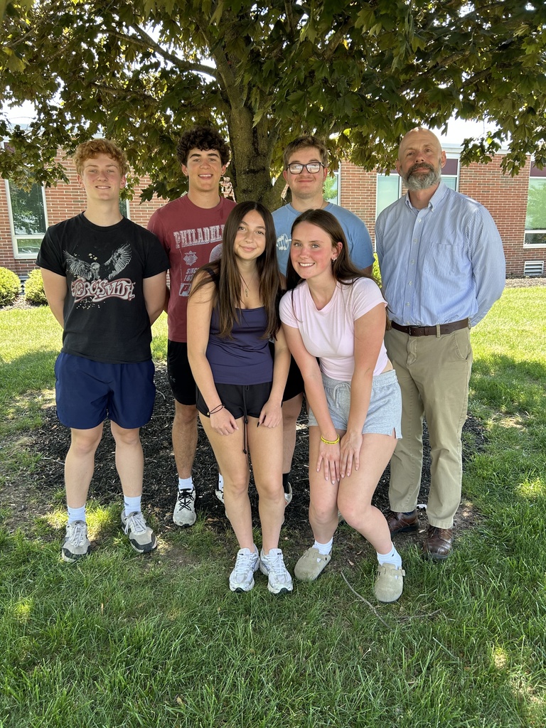 Picture of five students with their teacher on the grass outside of the high school standing in the shade of a tree.