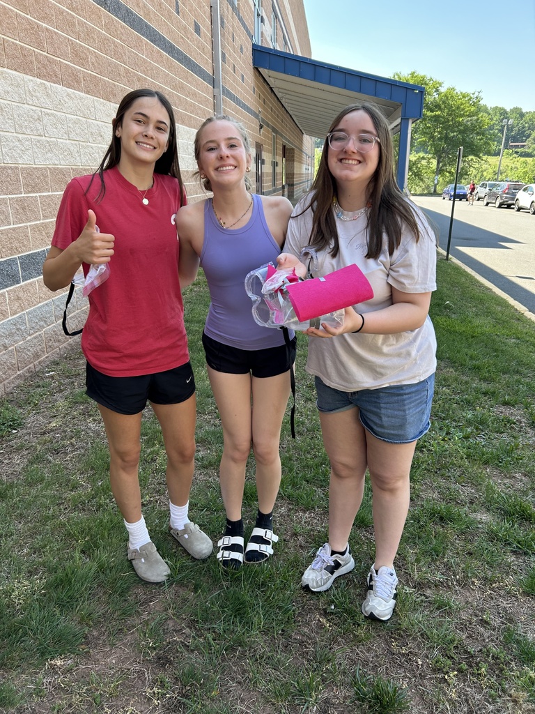 Three students standing outside holding their egg device one is displaying a thumbs up sign after their egg landed safely on the ground.