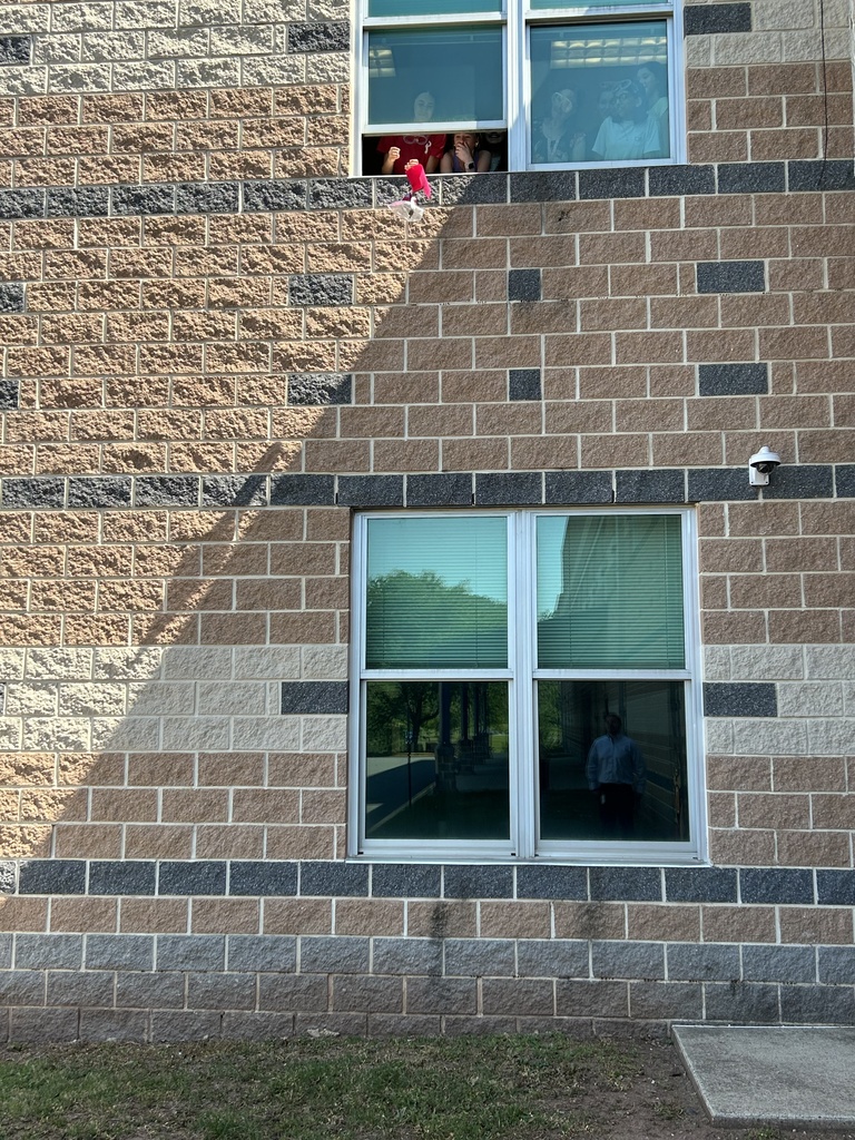 Egg in it's plastic bag/felt device being tossed out of a window from the second story of the school while students look on out of the window.