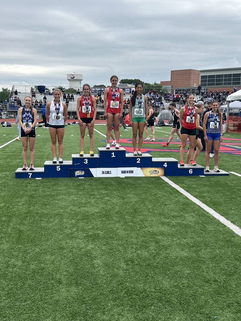Seven students standing on a football field on risers wearing medals.
