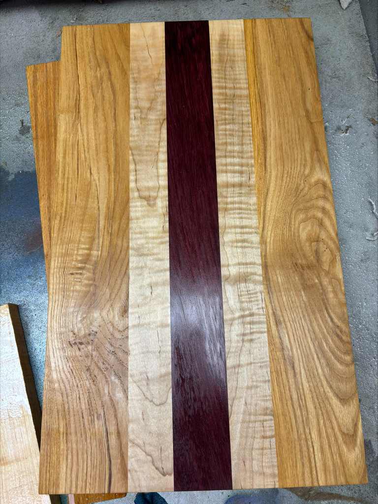 Serving board made with a combination of three different colored woods.  Medium oak, pine and cherry in a striped pattern with cherry being in the center flanked by two pine and then oak on the ends.