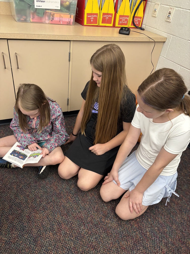 Three students sitting on a carpeted floor reading a book together.