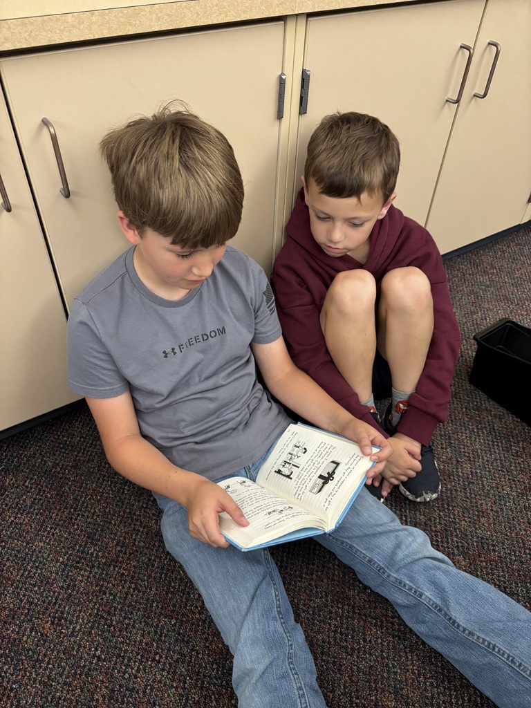 Two students sitting on a carpeted floor reading a book together.