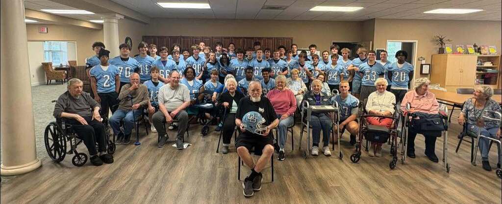 Entire football team pictured standing with residents of Keystone Villas who are seated in chairs in front of them.