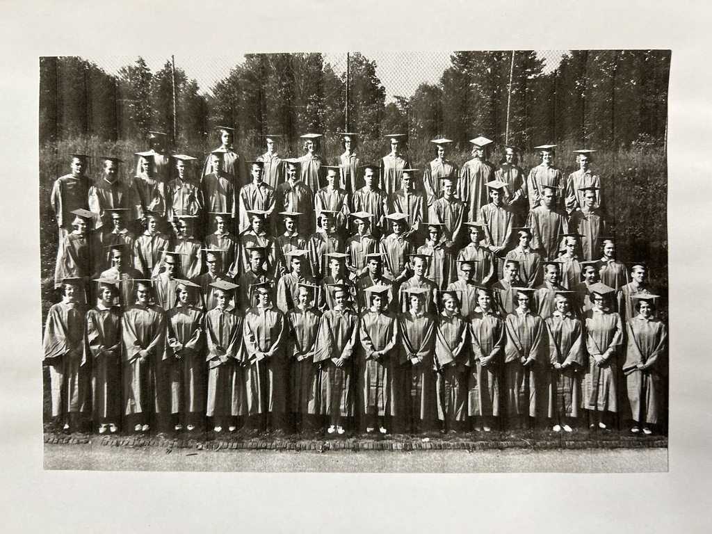 Black and white photo of a Daniel Boone School District graduating class of 69 students wearing caps and gowns standing in 5 rows on risers outside on the baseball field.