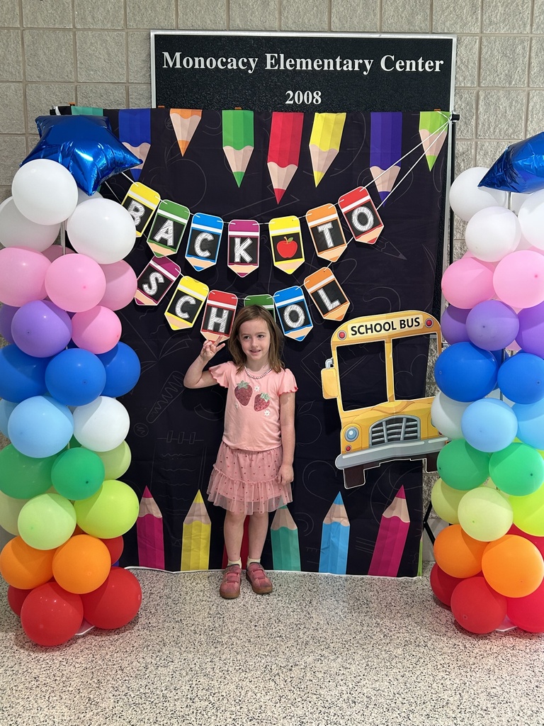 One student standing in front of a black fabric background with a Back to School Banner, school bus and colored pencils. Each side of the background has rainbow colored balloon towers with a blue mylar star balloon on top.