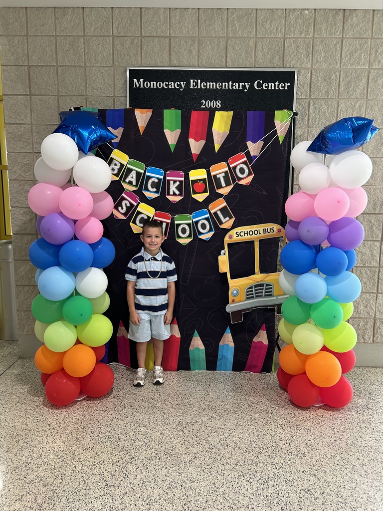 One student standing in front of a black fabric background with a Back to School Banner, school bus and colored pencils. Each side of the background has rainbow colored balloon towers with a blue mylar star balloon on top.
