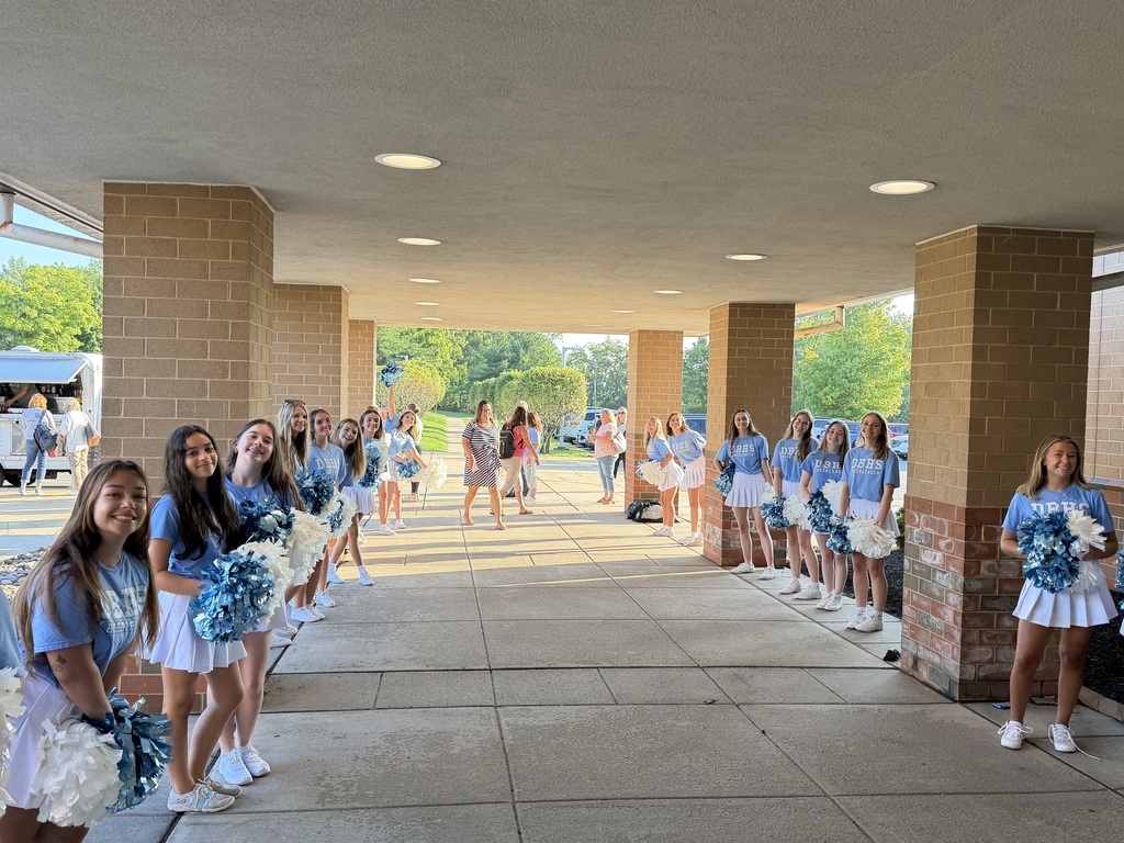DBAHS Cheerleaders in their blue tshirts and white skirts holding blue and white pom poms welcome staff outside of the middle school entrance.