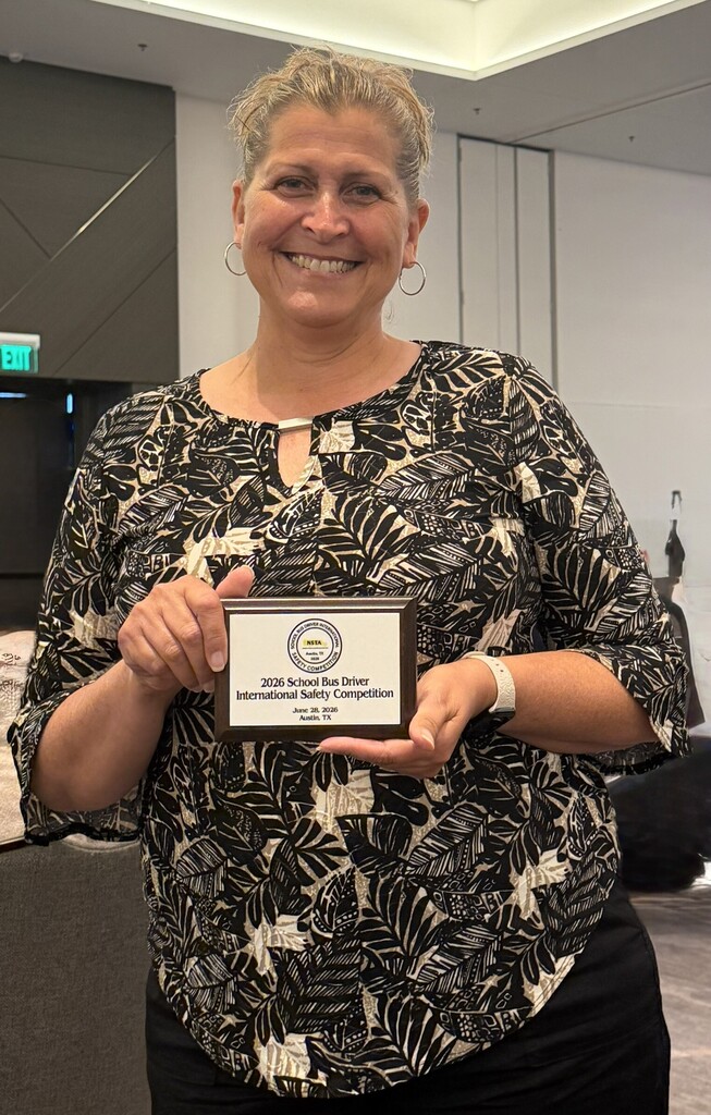 Pamela Little smiles while holding a plaque commemorating her participation in the 2026 School Bus Driver International Safety Competition in Austin, Texas.
