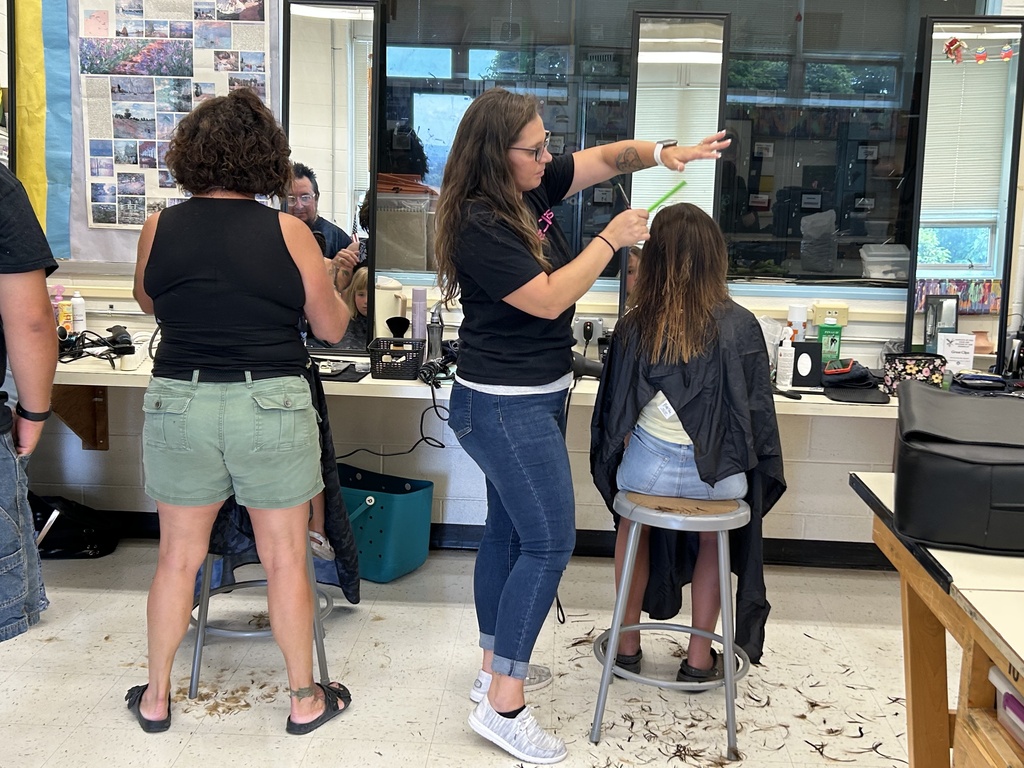 Picture of a stylist from Classic Elegance and one from Great Clips cutting students' hair.