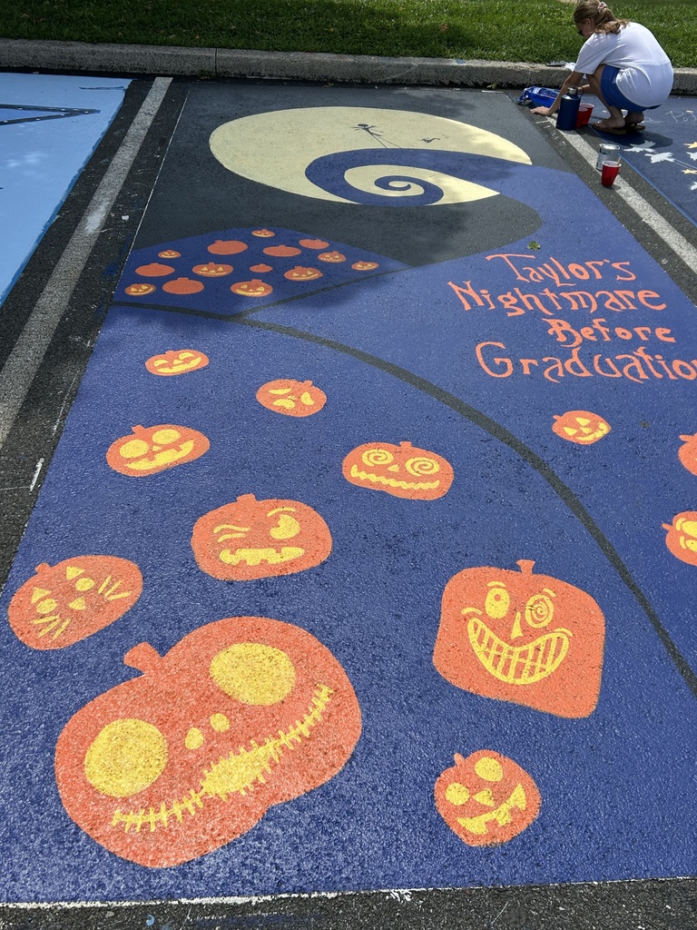 A freshly painted blue parking spot features a large yellow crescent moon, a dark blue spiral, and numerous orange pumpkins with playful jack-oβ-lantern faces. The words βTaylorβs Nightmare Before Graduationβ are painted in orange lettering.