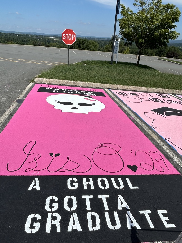 A completed parking spot features a bright pink background with a skull wearing a graduation hat, the name βIsis O '27,β large βA GHOUL GOTTA GRADUATEβ lettering in white on a black background..