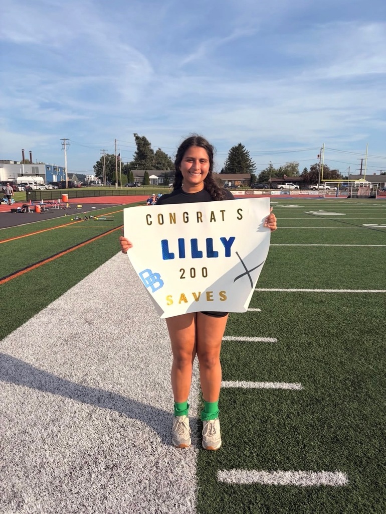 Daniel Boone field hockey player senior Lilly Maskeri holding a sign celebrating her 200 saves milestone. The player stands on the football field on a sunny day.