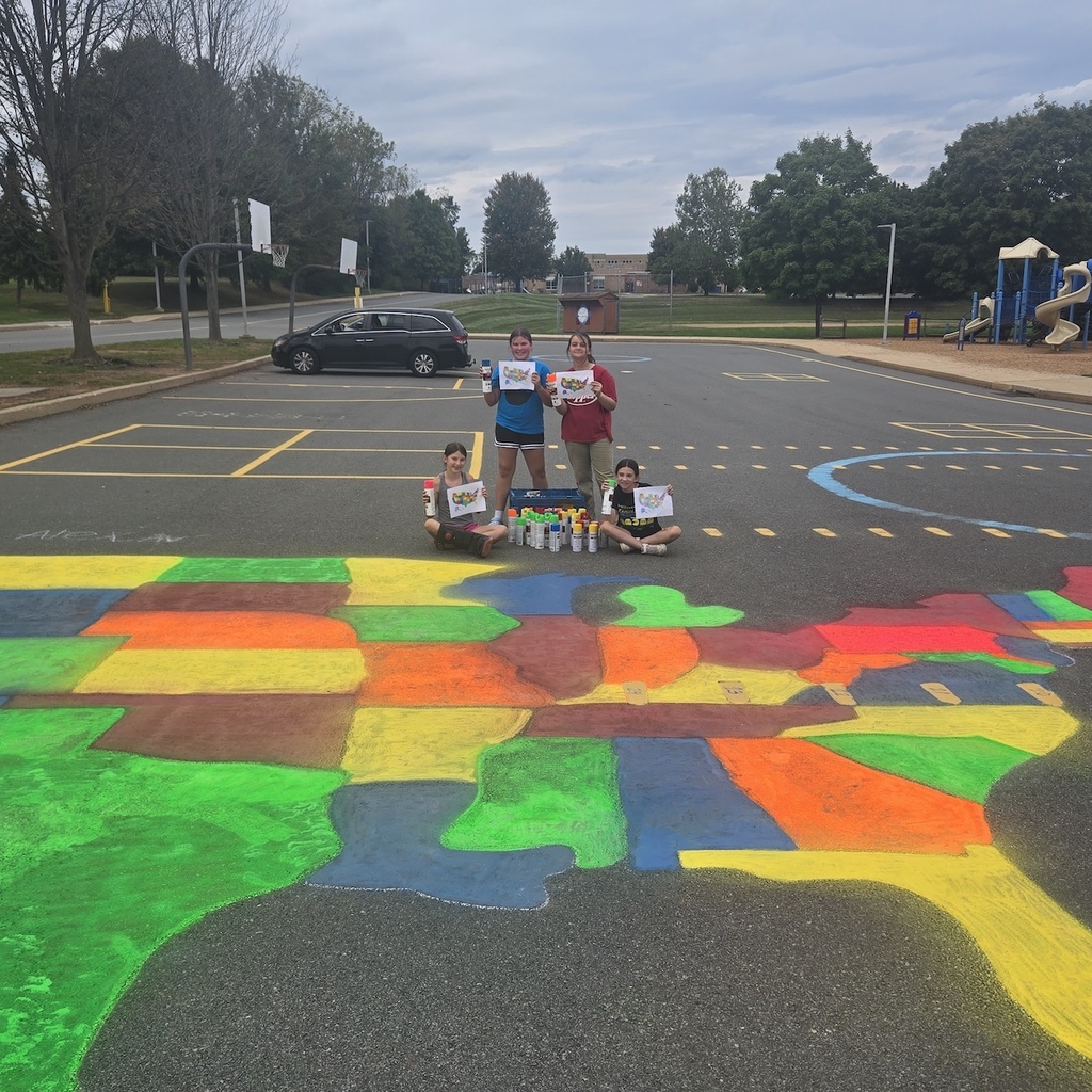 Four students holding colorful printed map page of the US with cans of fluorescent spray paint. Two girls are sitting on the playground and two girls are standing.