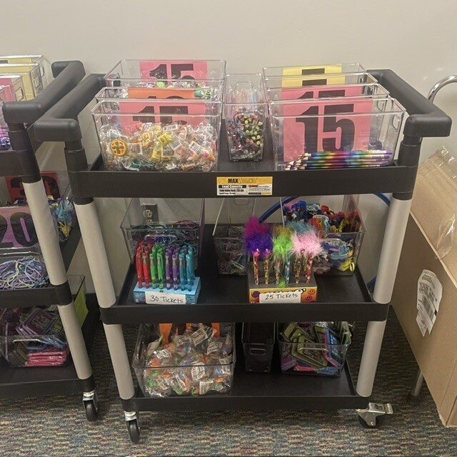 Wheeled three shelf cart with clear bins of prizes such as pencils, pens, fidgets and more.