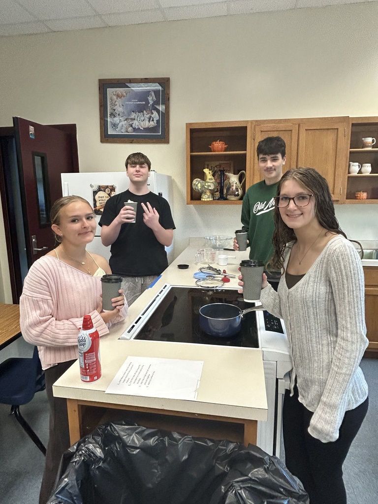 Four students are smiling at the camera while holding their disposable coffee cups with black lids.