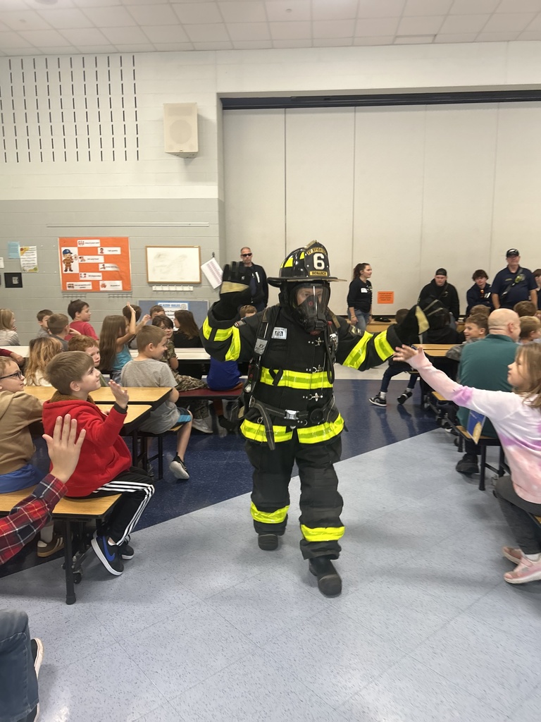Third grade teacher in full fire fighter uniform walking around the cafeteria giving high fives to students.