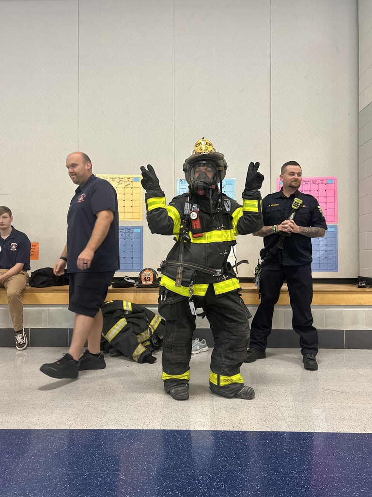 Paraprofessional in full fire fighter uniform holding up double peace signs.