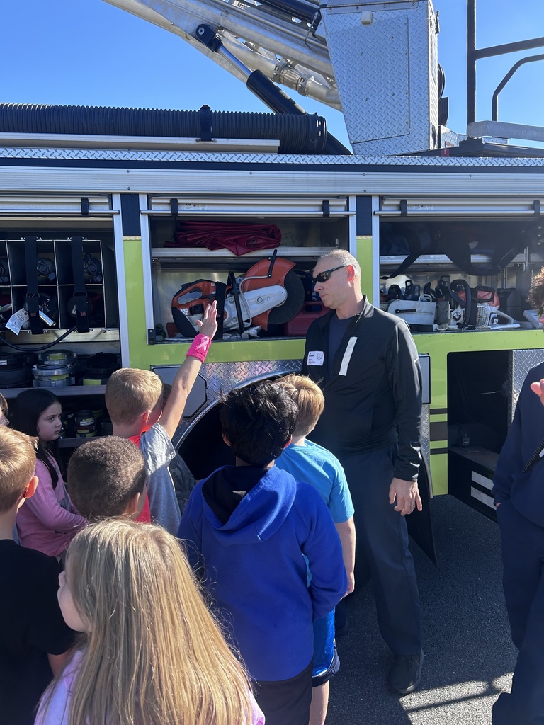 Photo of students asking fire fighter questions in front of the fire truck. One student has his hand raised.