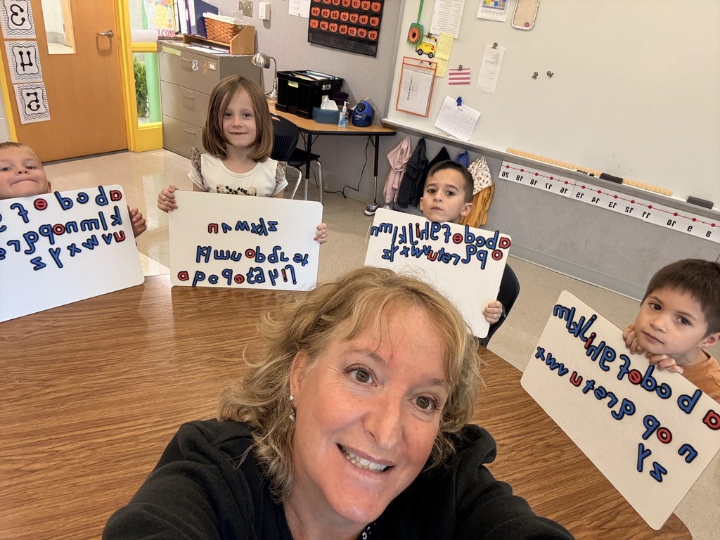 Mrs. Murray takes a selfie with her students who are seated at a table holding whiteboards with magnetic letters in alphabetical order