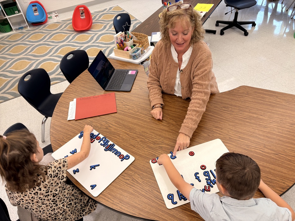Mrs. Murray works at a kidney shaped table to help students put magnetic letters into alphabetical order.