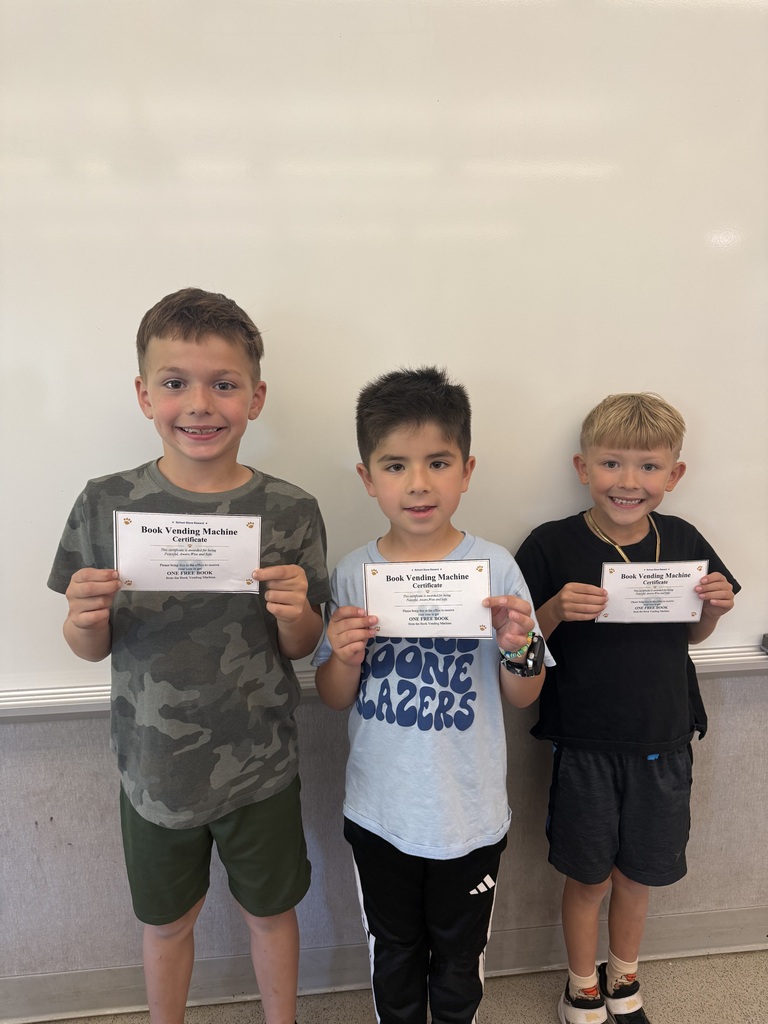 Three students proudly hold certificates they earned to redeem a free book from the Blazer Education Foundation’s Book Vending Machine.