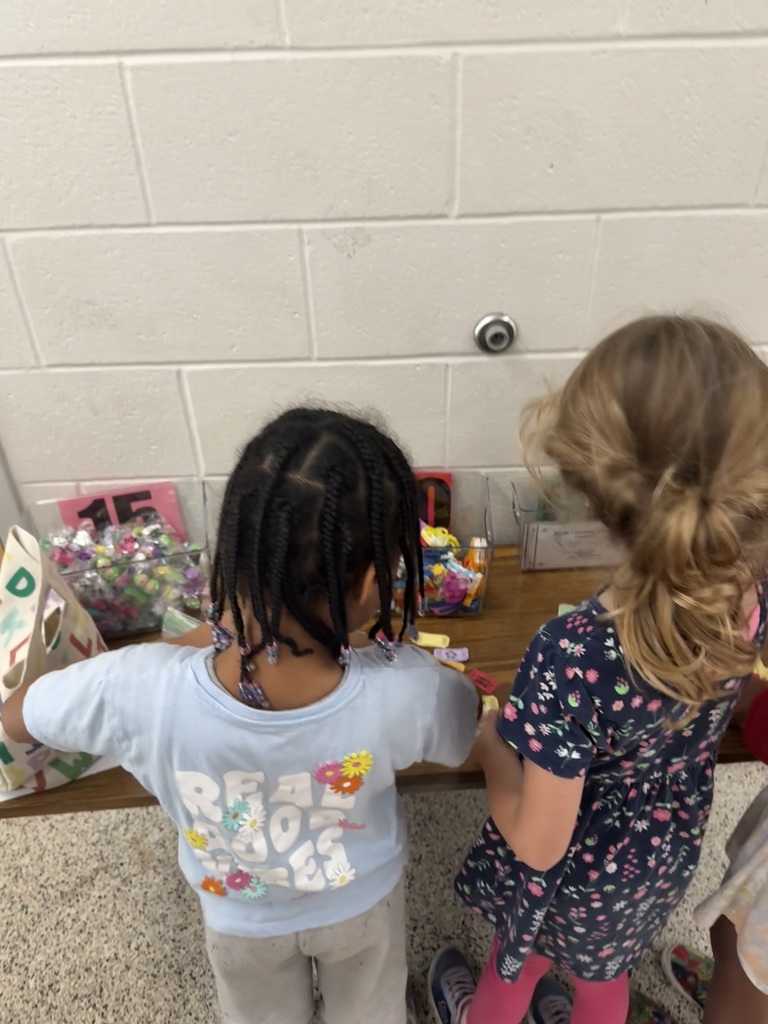 Two students shop for small items at the school store, choosing from a variety of colorful prizes and rewards.