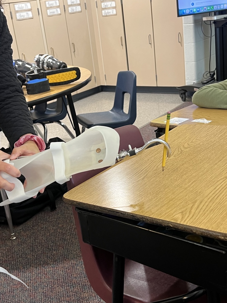 Picture of a prosthetic plastic arm piece with a curved metal attachment holding a pencil.