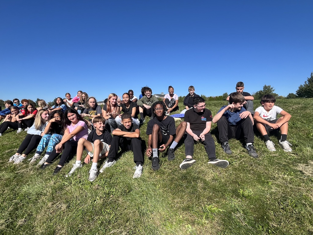 Large group of students sitting on a grassy hill.