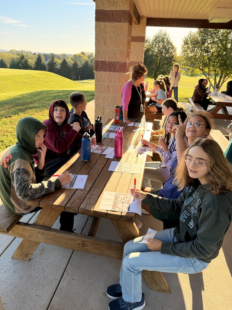 Students sitting at an outside picnic table playing bingo.