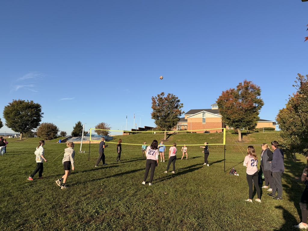 Students playing volleyball outside on a grassy field