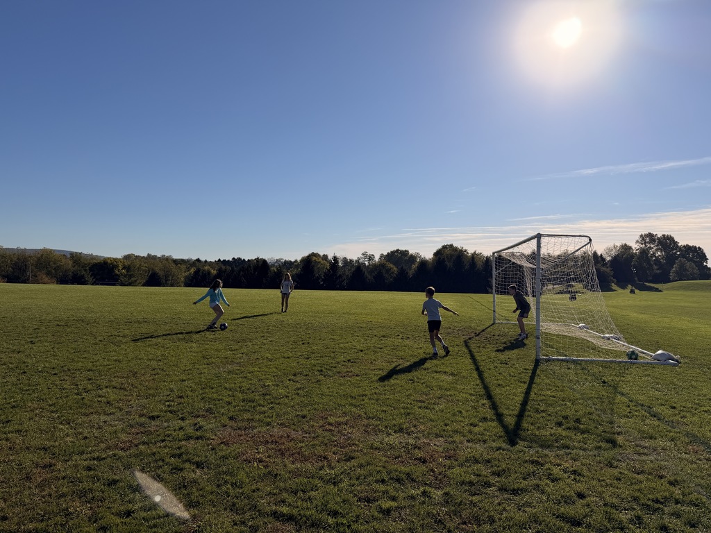 Students playing soccer outside on a grassy field.