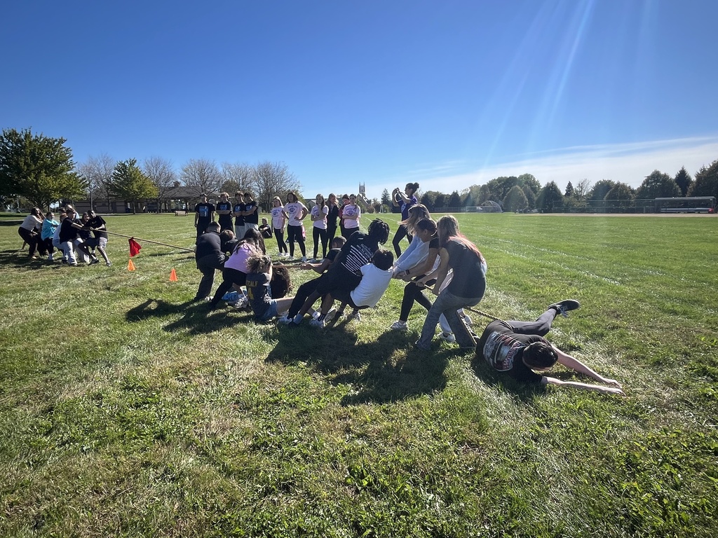 Students playing tug-of-war outside on a grassy field.