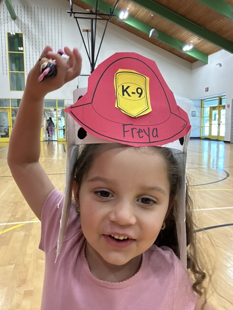 Picture of a student wearing a red paper firefighter hat with a yellow K-9 emblem and Dalmatian ears.