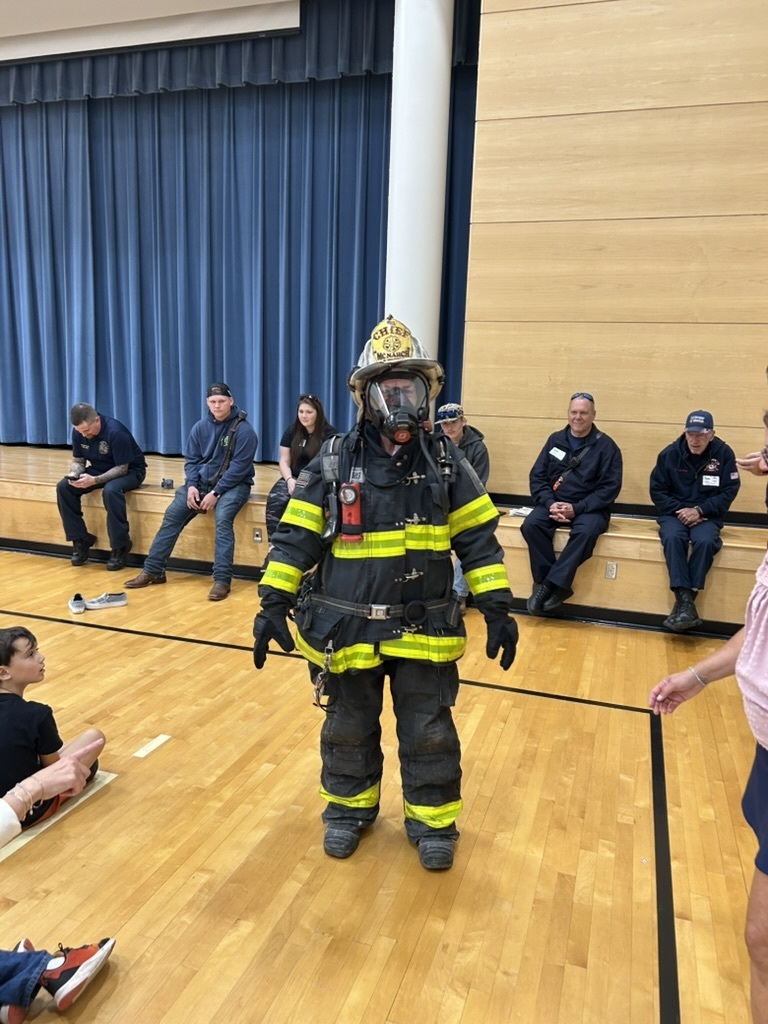 Teacher wearing a firefighter suit to show students that you should not be scared if a firefighter comes to help in case of emergency.
