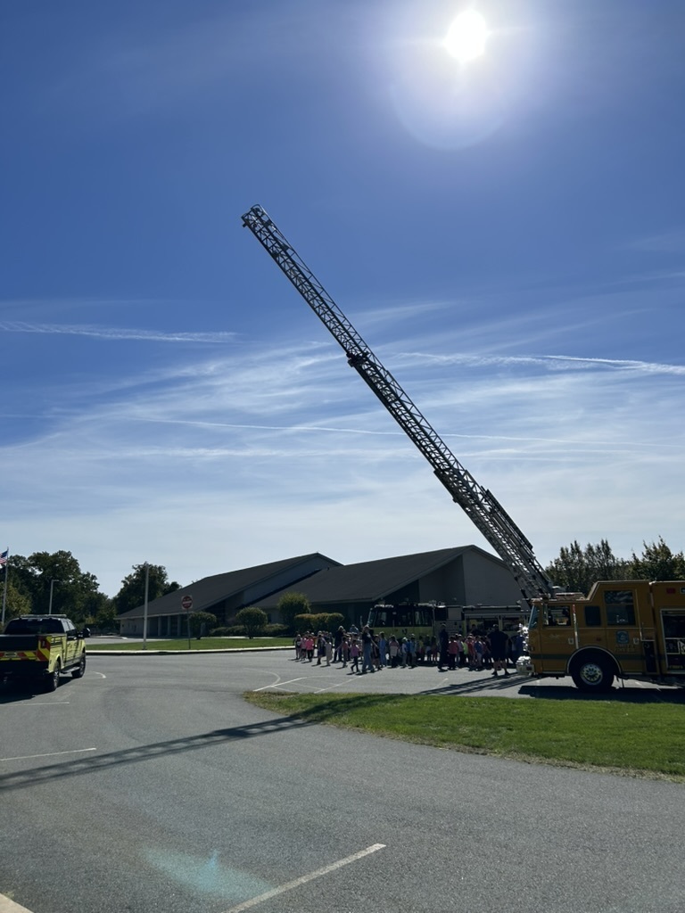 Firetrucks sitting on the parking lot while students and staff walk around to view them.