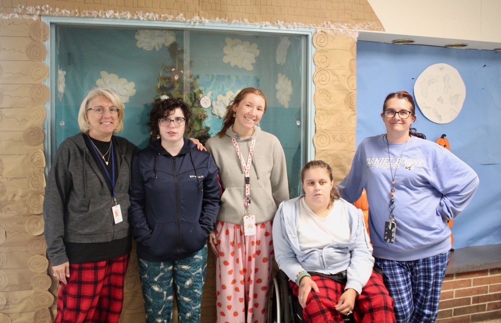 Students standing with aides one student in a wheel chair - all wearing pajamas.