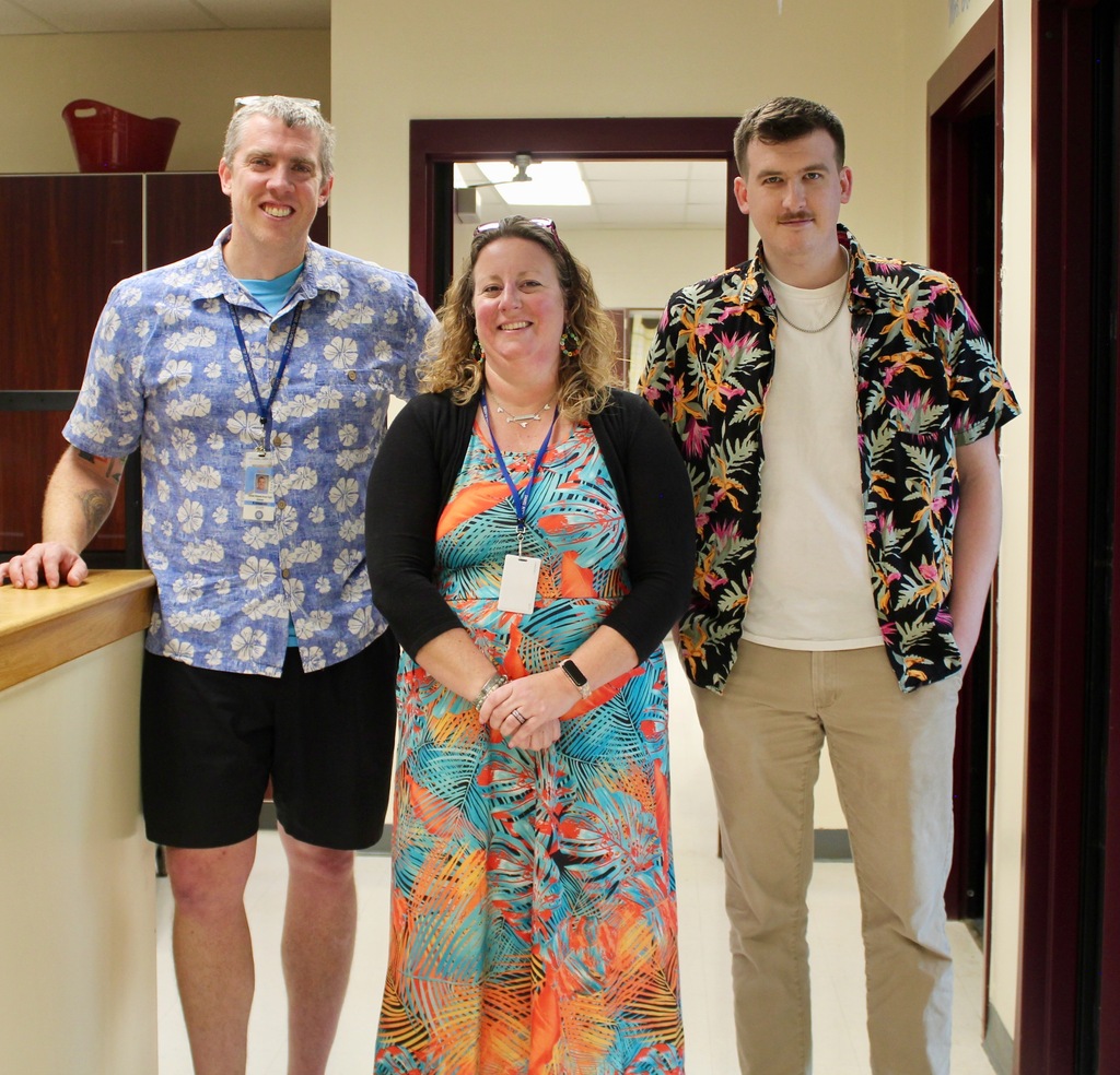 Three staff members - two men and one woman, show off their Hawaiian clothing