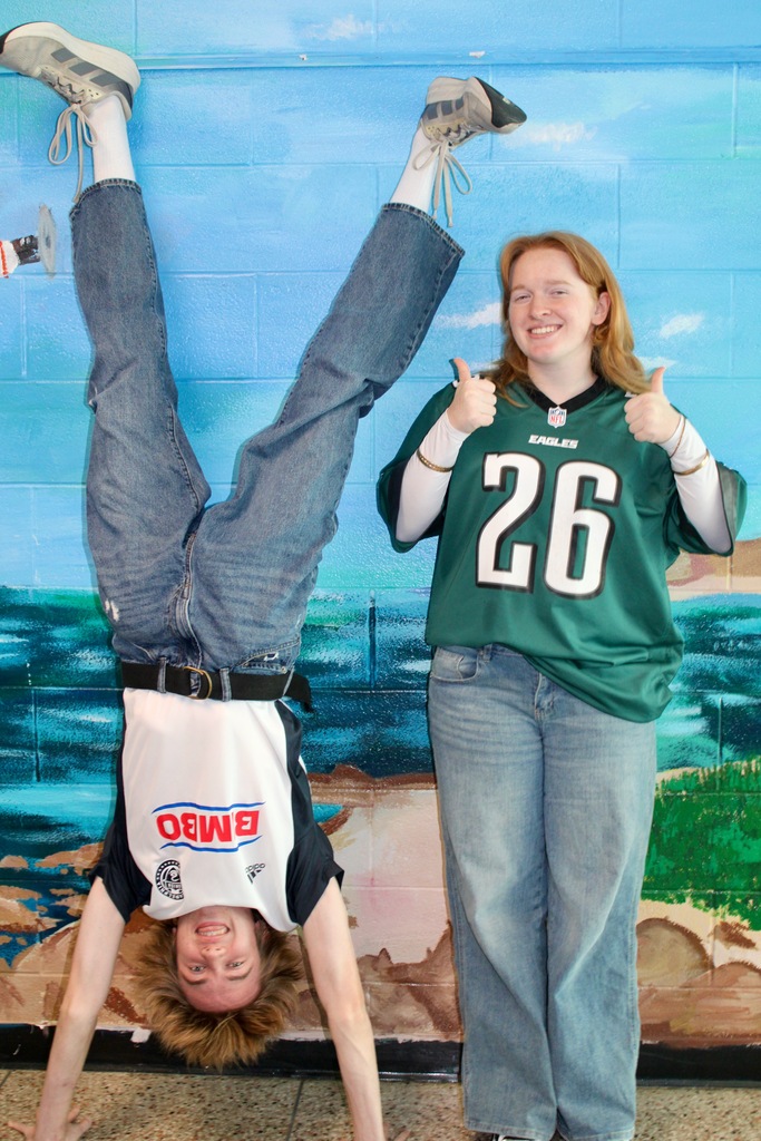 one student standing on hands wearing a BIMBO jersey, one student standing next to them wearing an Eagles jersey