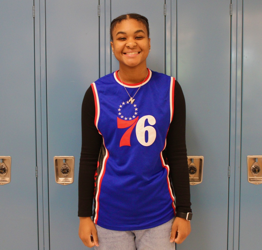 Student standing in front of blue lockers wearing a 76ers jersey