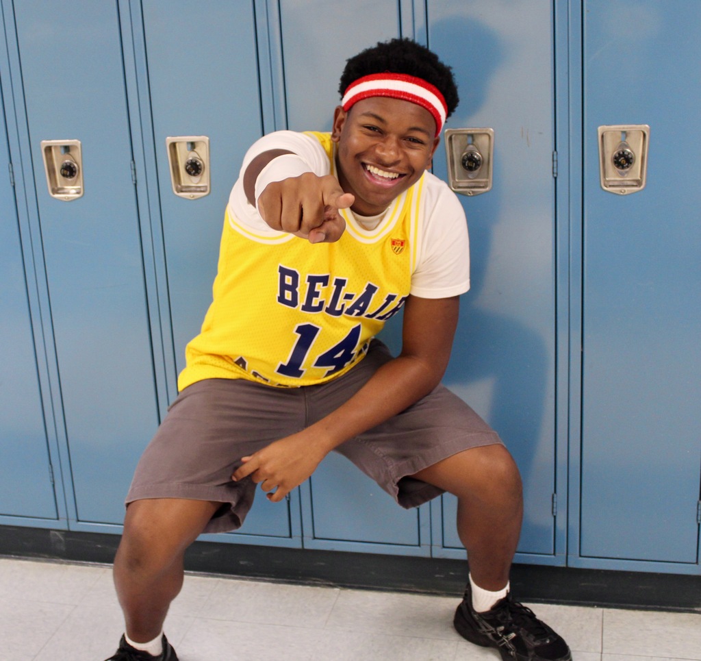 Student wearing a Bel-Air jersey crouching in front of blue lockers and pointing at the camera