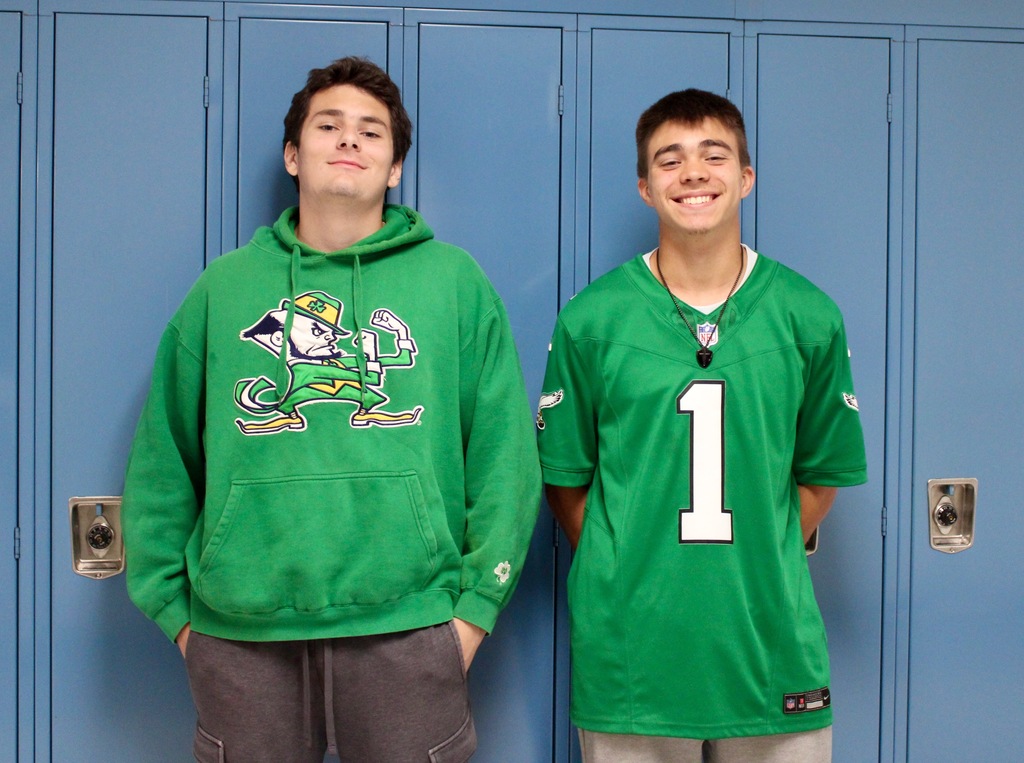 Two students standing in front of lockers - one wearing a Notre Dame sweatshirt. The other is wearing an Eagles jersey.