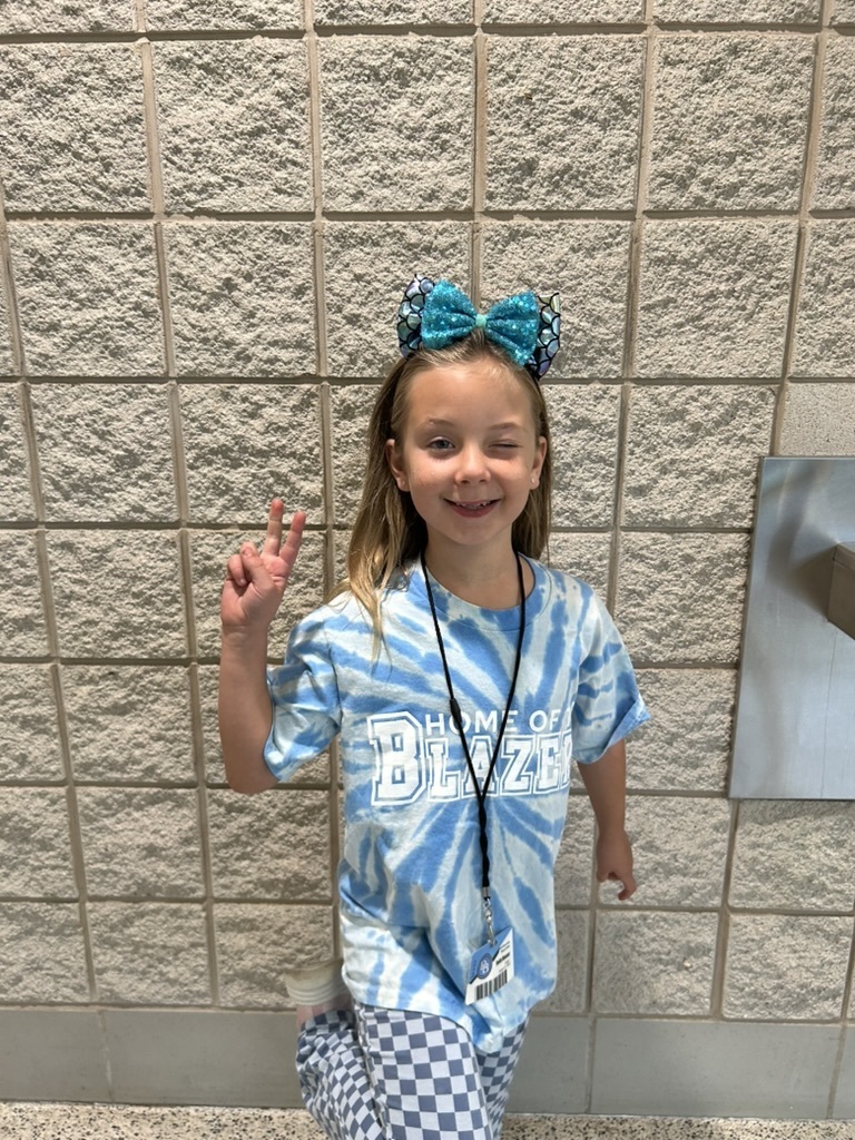 Student making a peace sign with her fingers wearing a tie-dyed Home of the Blazers t-shirt