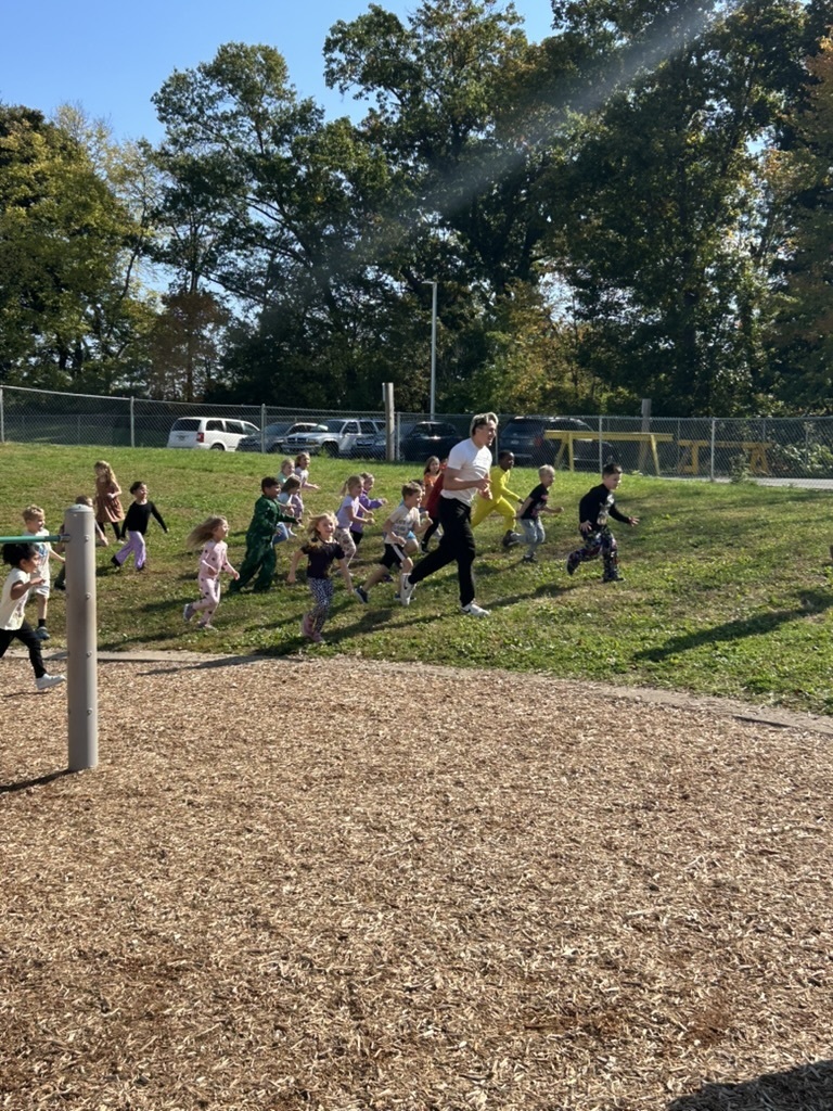 High school student running in the grassy area of the playground with about 20 students running with him.