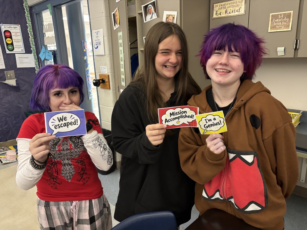 Three students smiling holding signs that say We Escaped, Mission Accomplished and I'm a Genius!