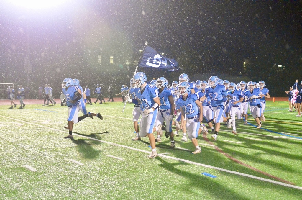 Football team runs onto the field carrying a DB flag in the rain